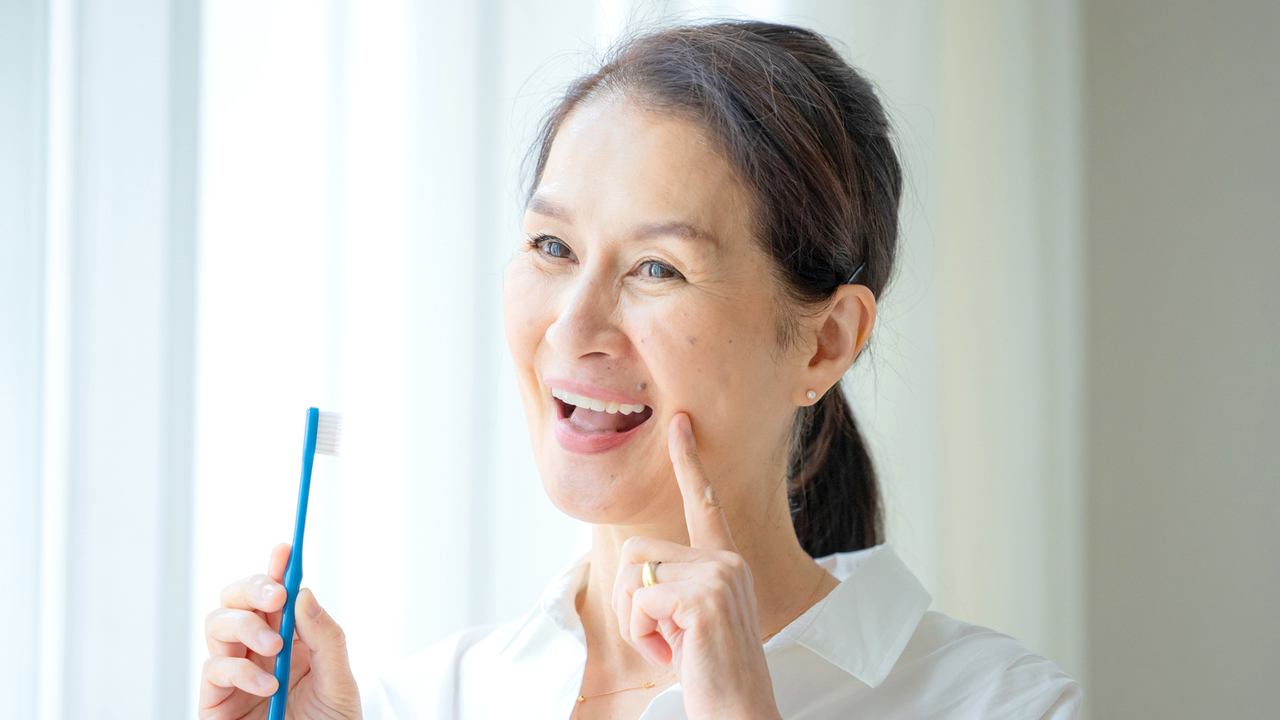 歯磨きをしながら歯並びをチェックする60代女性