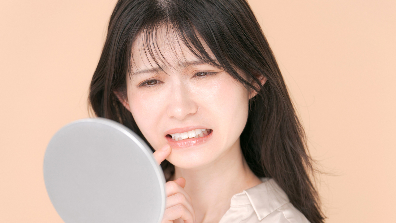 鏡を見ながら前歯の矯正が結婚式に間に合うか不安に思う女性