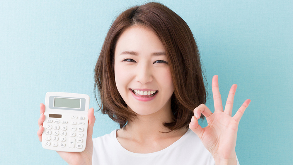 電卓を持った笑顔の女性が左手でオッケーマークを作っている画像