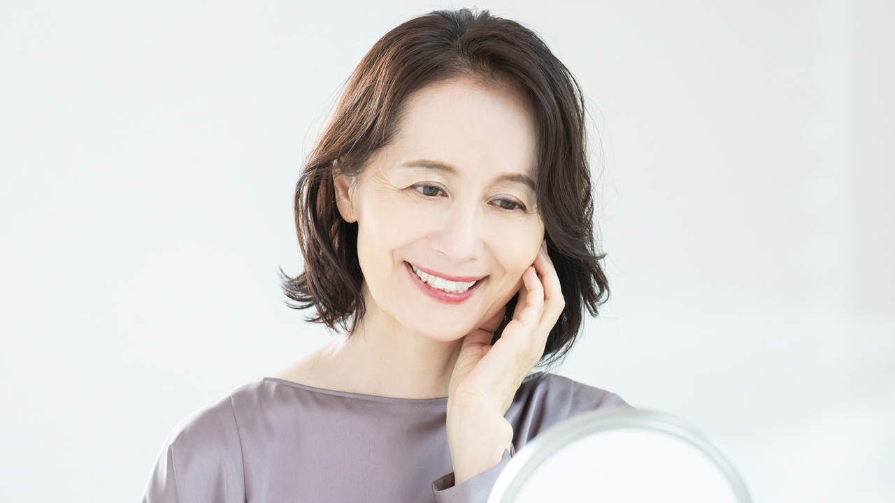 鏡で自分の歯並びを確認する60代女性