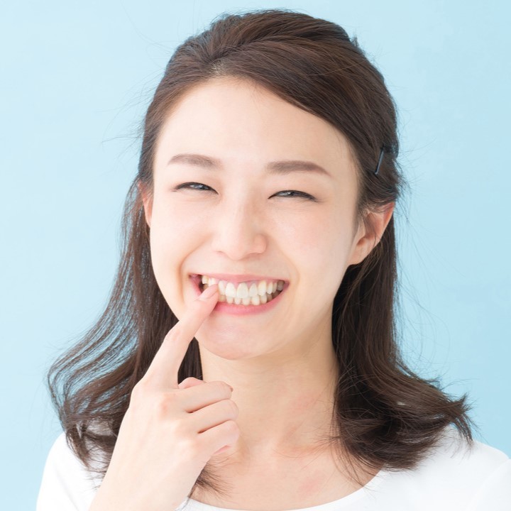 自分の前歯を指差している笑顔の女性