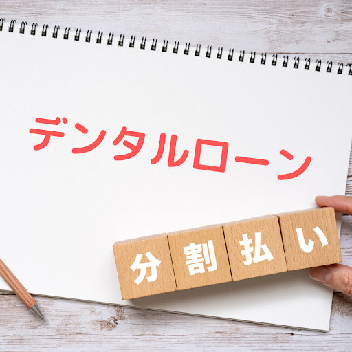 「デンタルローン」と書かれているスケッチブックと、その上に「分割払い」のブロックをつまんでいる指先が見える画像